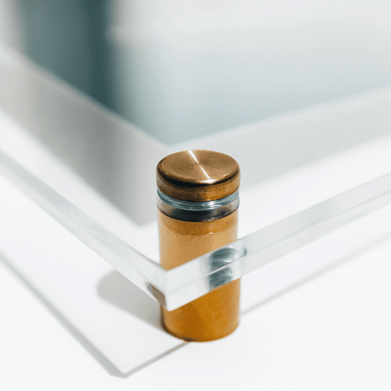 Closeup of 1 corner of a clear acrylic picture frame with gold accent hardware.