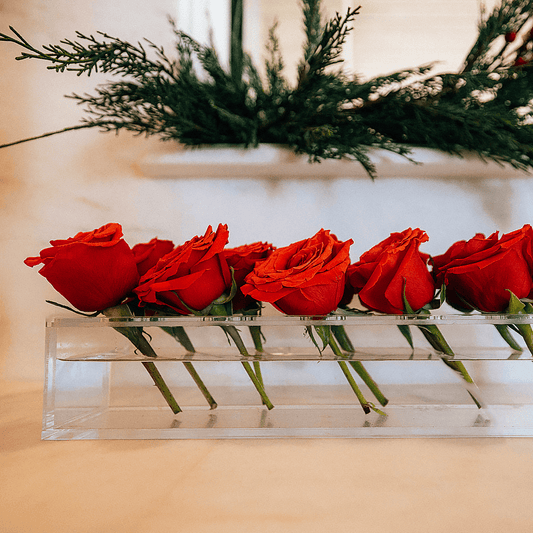 A clear acrylic horizontal short stem floral centerpiece displaying fresh cut red roses.