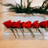 A clear acrylic horizontal short stem floral centerpiece displaying fresh cut red roses.