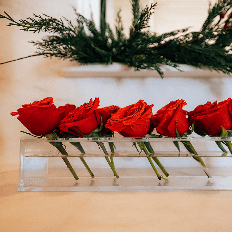 A clear acrylic horizontal short stem floral centerpiece displaying fresh cut red roses.
