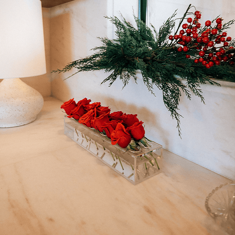 A clear acrylic horizontal short stem floral centerpiece displaying fresh cut red roses.
