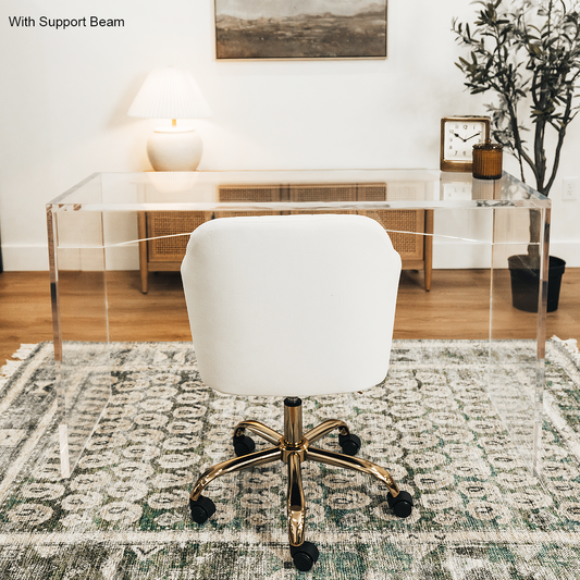 An acrylic lucite slab desk with a white chair in front, placed in an office setting with a painting on the wall and a tree in the background.