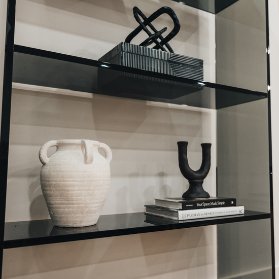Closeup of a vertical smoke gray acrylic 4 interior shelf bookcase decorated with vases, books, and decor placed against a white wall in a living room.