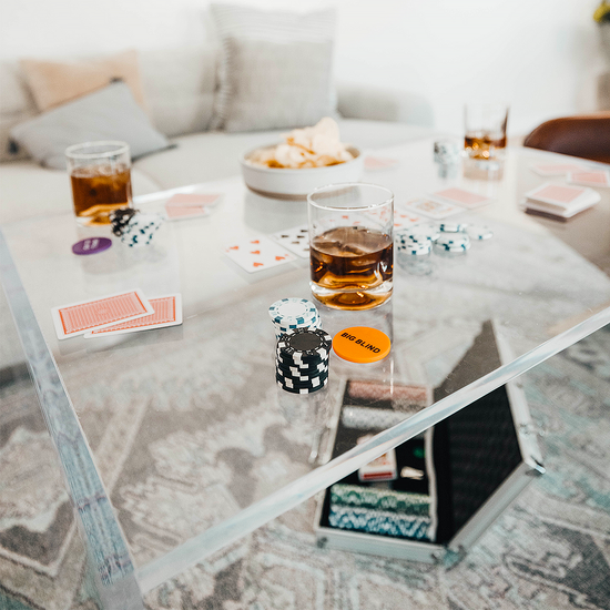 Closeup and top view of the corner edge looking down through a clear acrylic 23" slab coffee table displaying drink glasses, snacks, and a card game.