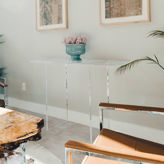 Clear acrylic lucite console table with a decorative vase and plant in a living room setting.
