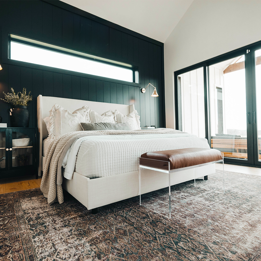 An elegant acrylic lucite brown leather upholstered bench at the foot of a bed in a stylishly decorated bedroom setting.