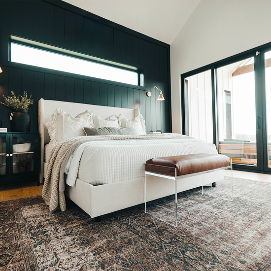 An elegant acrylic lucite brown leather upholstered bench at the foot of a bed in a stylishly decorated bedroom setting.