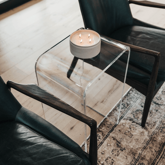 Clear acrylic waterfall edge end table displaying a candle placed in a living room between 2 chairs.