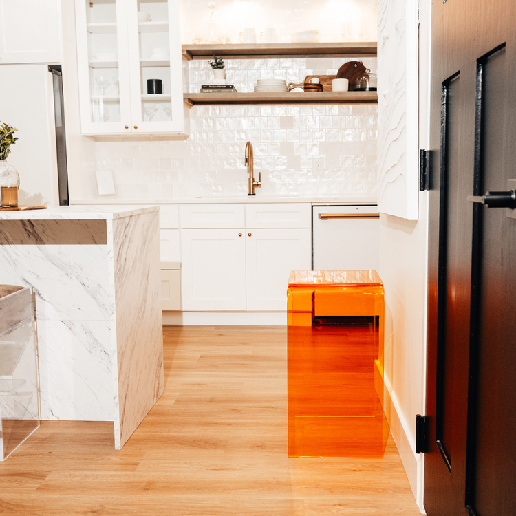 A orange tinted acrylic lucite waterfall edge side table against a wall in a kitchen. 