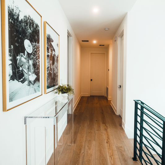 Clear acrylic slab entryway table placed in a hallway above a staircase to the 2nd story. Table has been decorated with a plant and is placed in front of 2 large family photos.