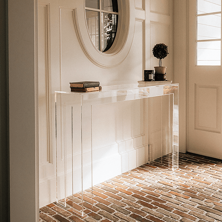 Modern clear acrylic console table against a white wall with decorative items placed in a brick floor foyer.