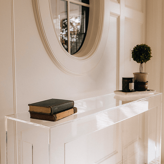 Modern clear acrylic console table against a white wall with decorative items placed in a brick floor foyer.