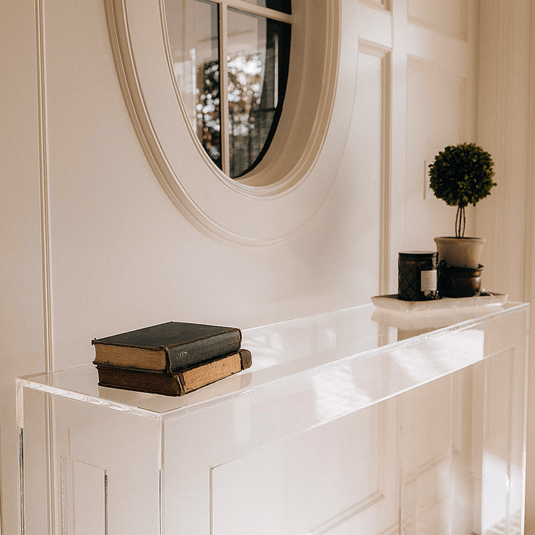 Modern clear acrylic console table against a white wall with decorative items placed in a brick floor foyer.