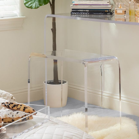 Closeup of a clear acrylic vanity stool next to its partnering vanity table in a bedroom. 