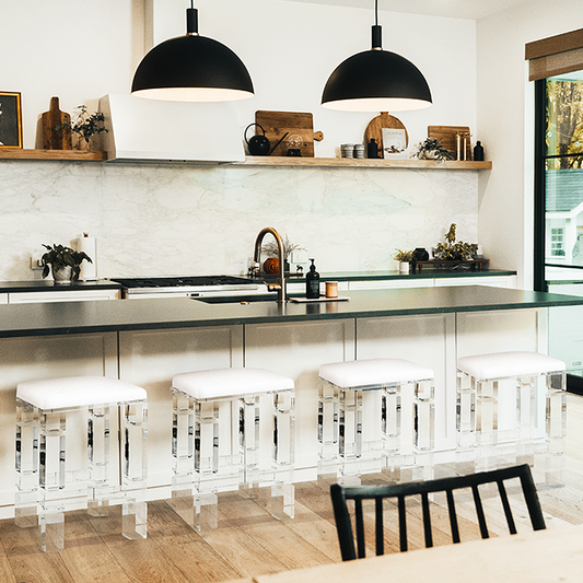  4 clear acrylic lucite barstools with white padded seats placed at a kitchen island.