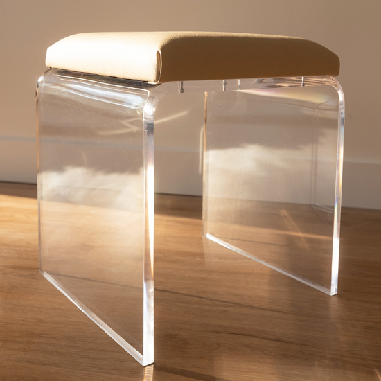 A closeup of a single acrylic ottoman chair with brown leather upholstery. 