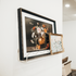 Framed floral artwork on a white wall being held by a clear acrylic floating bookshelf with a wavy edge. 