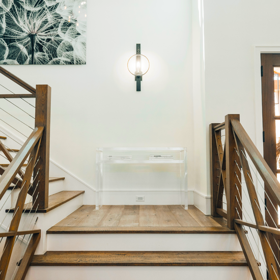 A clear acrylic console table with books on the interior shelf placed on a landing of a wooden staircase.