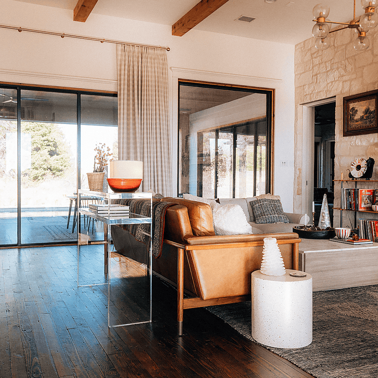 A clear acrylic console table with books on the interior shelf and decor on top placed behind a couch in a living room setting.
