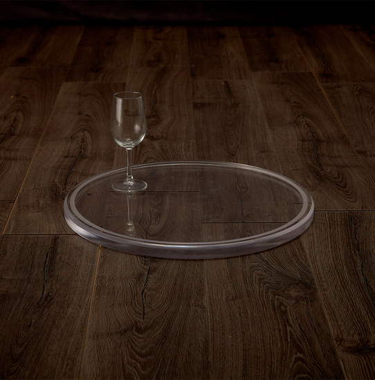 Catalog view of a clear acrylic round centerpiece tray displaying 1 wine glass for size comparison placed on a hardwood table.