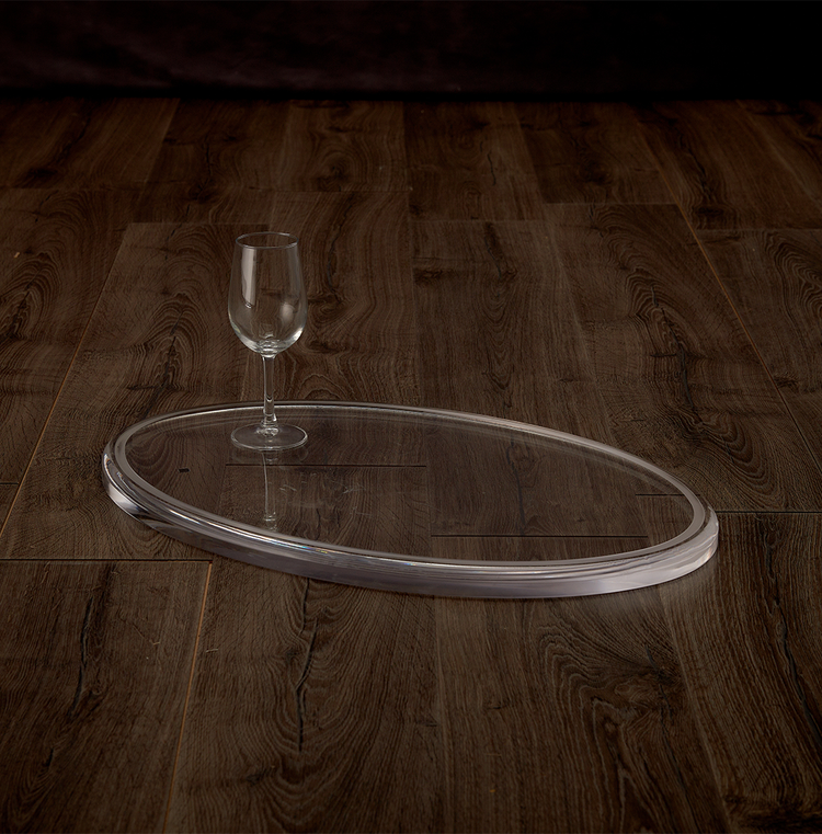 Catalog view of a clear acrylic oval centerpiece displaying 1 wine glass for size comparison on a hardwood table.