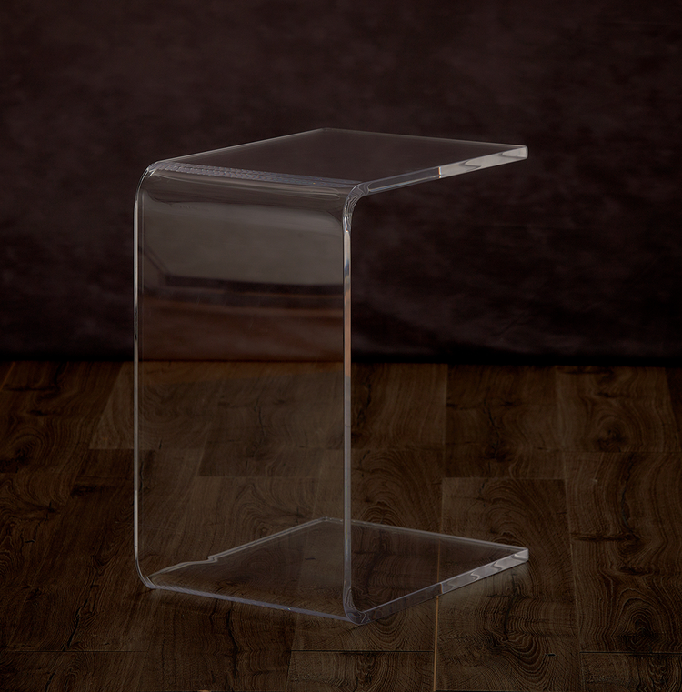 Catalog view of a clear acrylic open end, c-shaped end table on a hardwood floor.