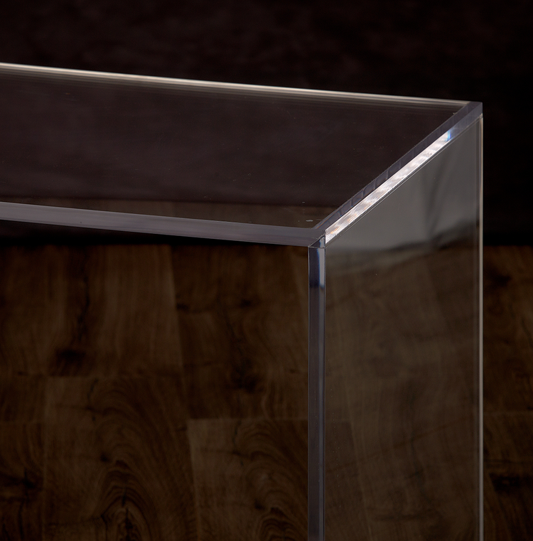 Catalog closeup of the top corner edge on a clear acrylic slab desk or coffee table.