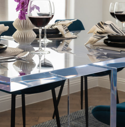 Closeup of the edge of a clear acrylic slab style dining room table displaying a flower vase centerpiece, wine glasses and place settings.