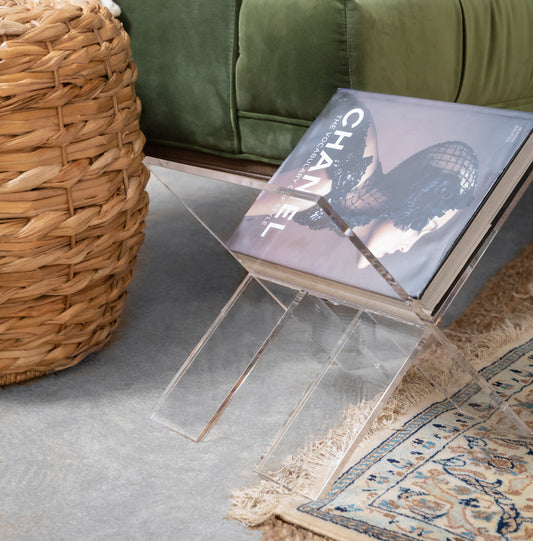 Clear acrylic X design magazine rack displaying a book next to a couch in a living room.