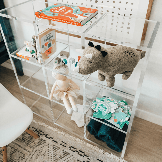 Top view of a clear acrylic 9 cube storage unit displaying children's toys, blankets, and books in a child's bedroom. The unit features 3 rows of 3 cubes.