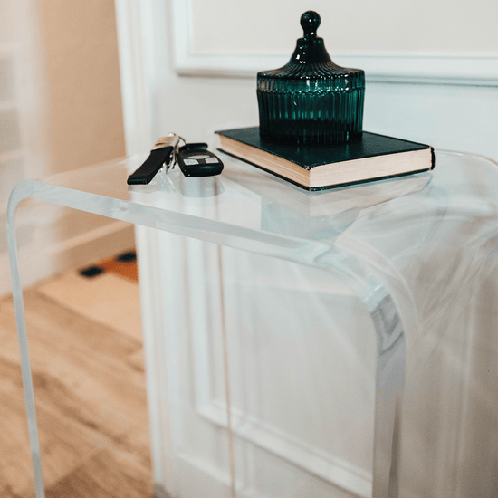 Closeup of the top and waterfall edge on a clear acrylic end table displaying car keys, a book and a decorative dish.